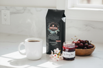 Pops Coffee Company Michigan Cherry bag on white marble with steaming coffee, fresh cherries and cherry blossoms