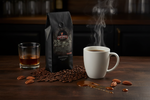 Pops Coffee Company Bourbon Pecan Torte bag on a dark wood bar with steaming coffee, bourbon in a rocks glass and caramel drizzle